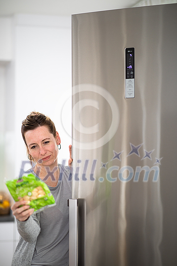 Pretty, young woman taking groceries out of the fridge, checking the dates, healthy eating concept, household lifestyle concept Pretty, young woman taking groceries out of the fridge, checking the dates, healthy eating concept, household lifestyle concept