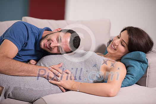Happy future dad listening the belly of his pregnant wife while relaxing on sofa at home