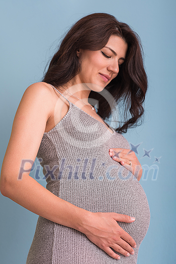 Portrait of happy pregnant woman with hands on belly isolated over blue background