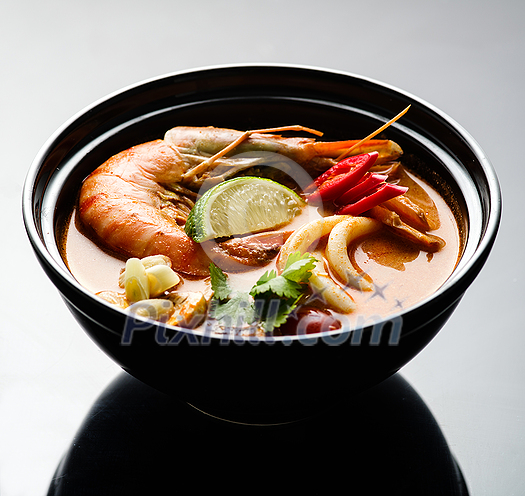 Tom Yam soup with seafood in a black plate Tom Yam soup with seafood in a black plate