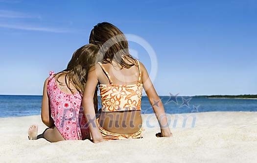 Two girls sitting on the sand looking at the sea Two girls sitting on the sand looking at the sea