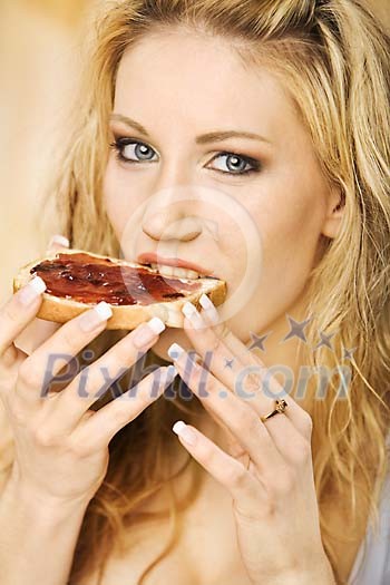 Woman taking a bite of white bread with jam on it Woman taking a bite of white bread with jam on it