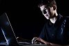 Teenage boy sitting with a laptop in a dark room