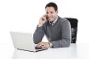 Clipped image of a businessman sitting behind the desk and typing on a computer while talking to a phone