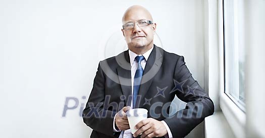 Businessman by window holding a cup of coffee Businessman by window holding a cup of coffee