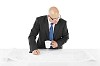 Man holding pen and coffee while working on a big blueprint