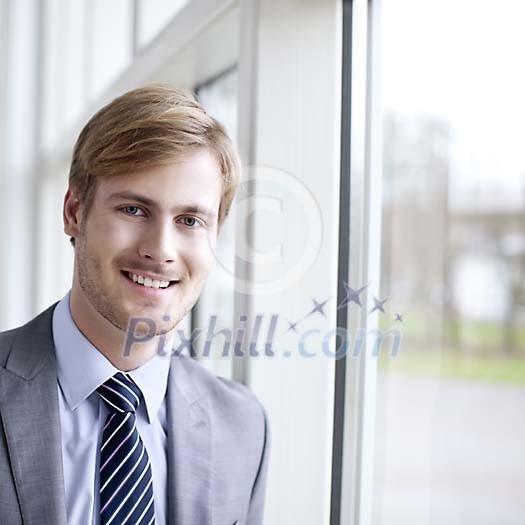 Smiling businessman standing next to a window Smiling businessman standing next to a window
