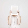 Woman hiding her face behind a tablet computer