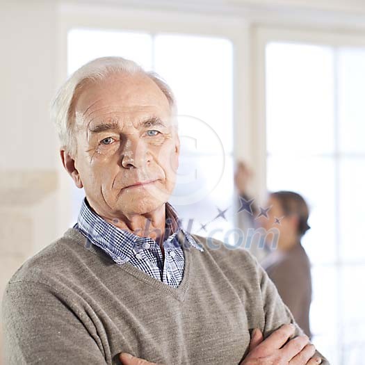 Senior man looking at camera, spouse unfocused on the background Senior man looking at camera, spouse unfocused on the background