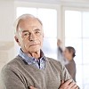 Senior man looking at camera, spouse unfocused on the background