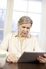 Senior woman reading at home from tablet computer