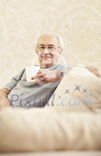 Older male sitting on the sofa, having coffee