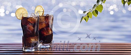 Glasses of soft drink on a table by a blue lake Glasses of soft drink on a table by a blue lake