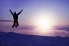 Person jumping on top of a mountain above the clouds