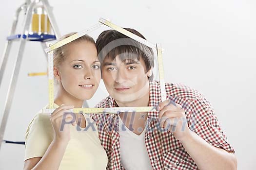 Couple looking through folding ruler shaped as a house Couple looking through folding ruler shaped as a house