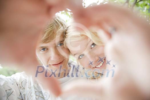 Couple looking through a heart shape made with their hands Couple looking through a heart shape made with their hands