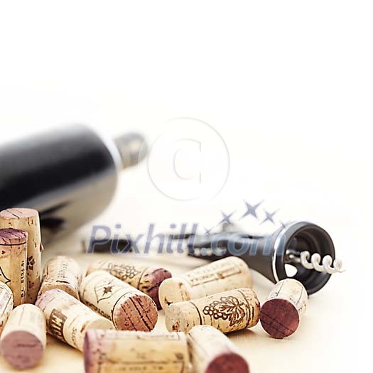 Red wine bottle, corkscrew and corks in shallow focus