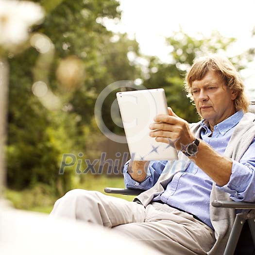Middle aged man sitting outside, holding ipad Middle aged man sitting outside, holding ipad