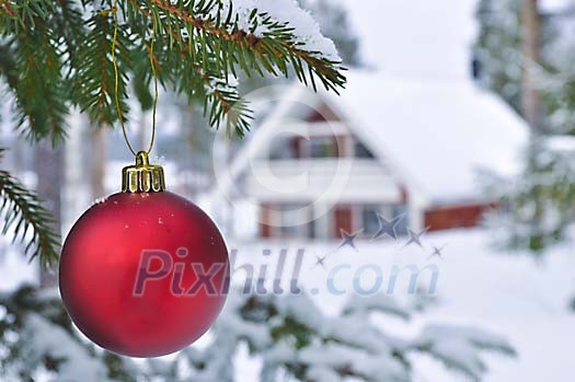 A red christmas ball in front of a house in snow