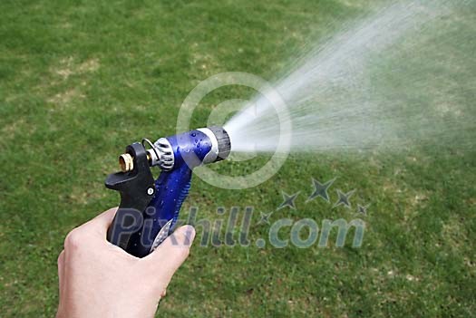 Hand holding the hose and watering the grass Hand holding the hose and watering the grass