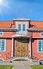 Red and grey stone house with red tiles and a blue sky with sunshine