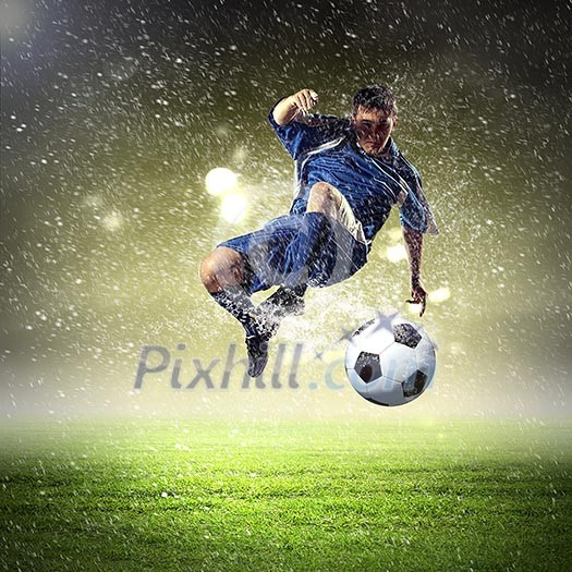 football player in blue shirt striking the ball aloft at the stadium under the rain