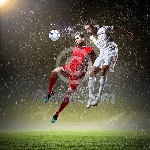 Two football players in jump to strike the ball at the stadium Two football players in jump to strike the ball at the stadium