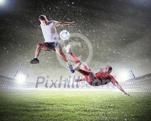 Two football players in jump to strike the ball at the stadium Two football players in jump to strike the ball at the stadium