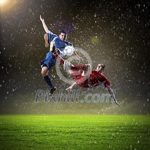 Two football players in jump to strike the ball at the stadium Two football players in jump to strike the ball at the stadium