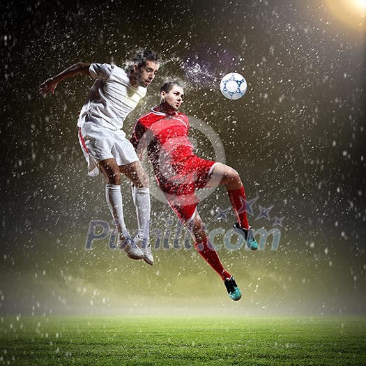 Two football players in jump to strike the ball at the stadium Two football players in jump to strike the ball at the stadium
