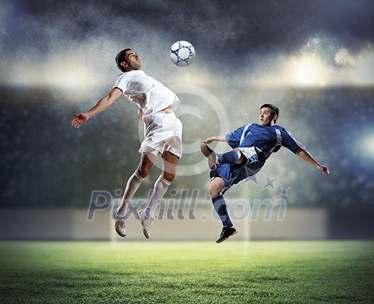 Two football players in jump to strike the ball at the stadium Two football players in jump to strike the ball at the stadium