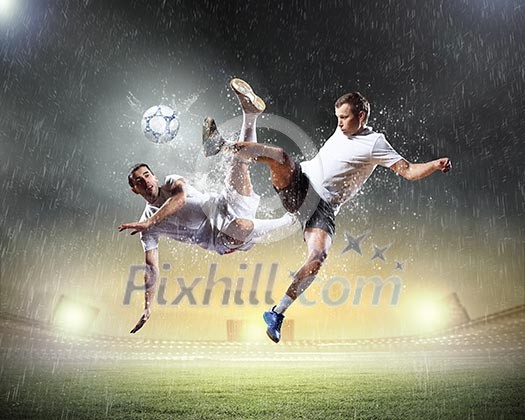 Two football players in jump to strike the ball at the stadium Two football players in jump to strike the ball at the stadium