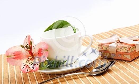 White cup with pink flowers and small gifts on a light table. White cup with pink flowers and small gifts on a light table.