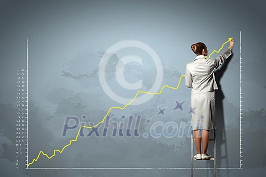 businesswoman standing on ladder drawing diagrams and graphs on wall businesswoman standing on ladder drawing diagrams and graphs on wall