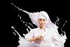 Asian female cook against milk splashes in red apron against black background holding glass of milk