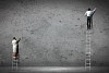 businesspeople standing on ladder drawing diagrams and graphs on wall