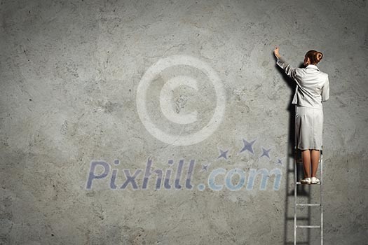 Businesswoman standing on ladder drawing diagrams and graphs on wall Businesswoman standing on ladder drawing diagrams and graphs on wall