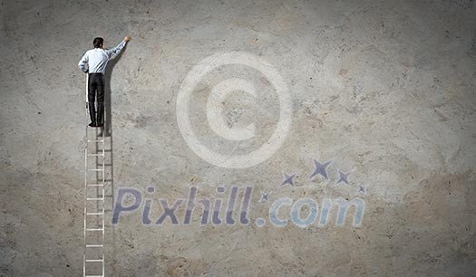 businessman standing on ladder drawing diagrams and graphs