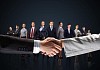 business handshake against black background and standing businesspeople