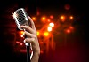 Female hand holding a single retro microphone against colourful background