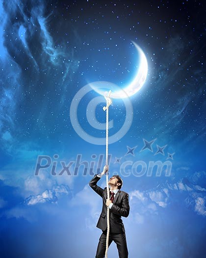Image of businessman climbing rope attached to moon Image of businessman climbing rope attached to moon