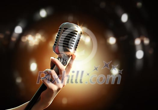 Female hand holding a single retro microphone against colourful background Female hand holding a single retro microphone against colourful background