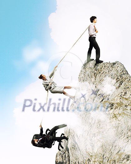 Image of three businesspeople pulling rope atop of mountain