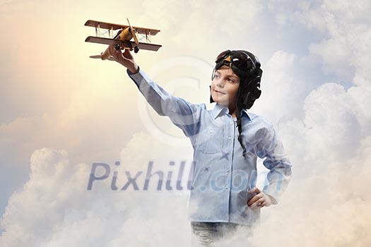 Image of little boy in pilots helmet playing with toy airplane against clouds background Image of little boy in pilots helmet playing with toy airplane against clouds background
