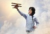 Image of little boy in pilots helmet playing with toy airplane against clouds background