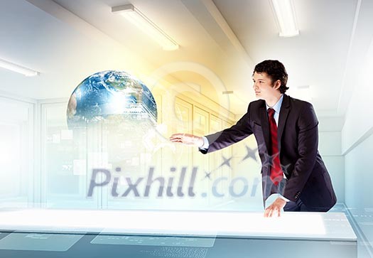 Image of young businessman clicking icon on high-tech picture of globe Image of young businessman clicking icon on high-tech picture of globe