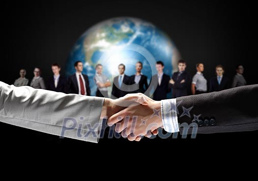 business handshake against black background and standing businesspeople business handshake against black background and standing businesspeople