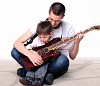 A young father teaches his young son to play guitar