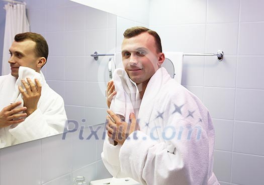 young man in bathroom wearing white bathrobe young man in bathroom wearing white bathrobe
