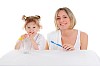 young mother and her young daughter brush their teeth on a white background